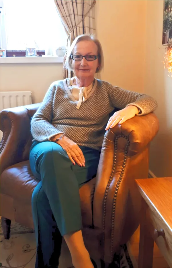 Helen O'Brien, smiling, sitting in a leather armchair in her counselling room
